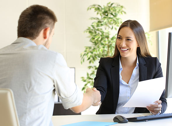 Man and woman in business casual shaking hands over a desk.