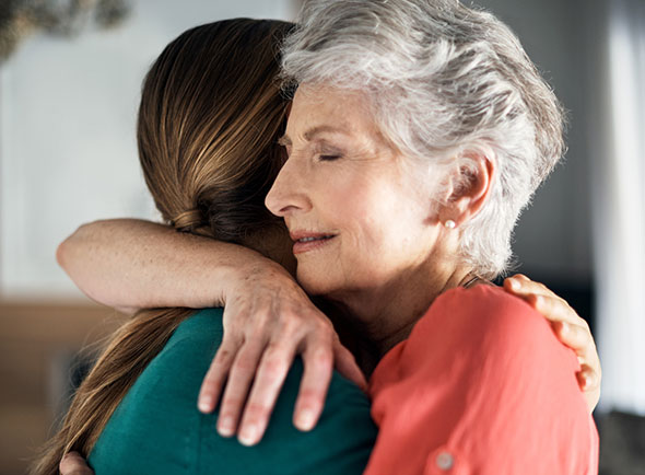 Older woman with eyes closed hugging younger woman.